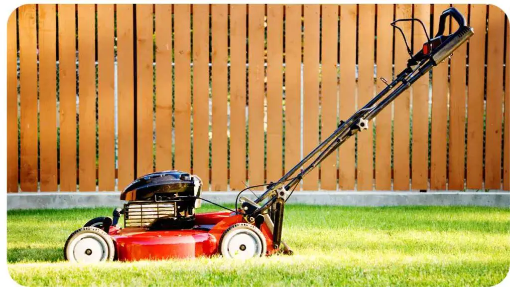 a red lawn mower sitting on the grass in front of a wooden fence