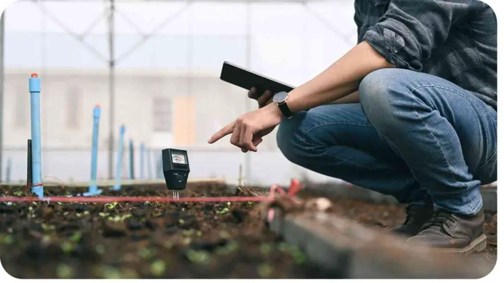 a person is kneeling down in a greenhouse with a digital thermometer in their hand