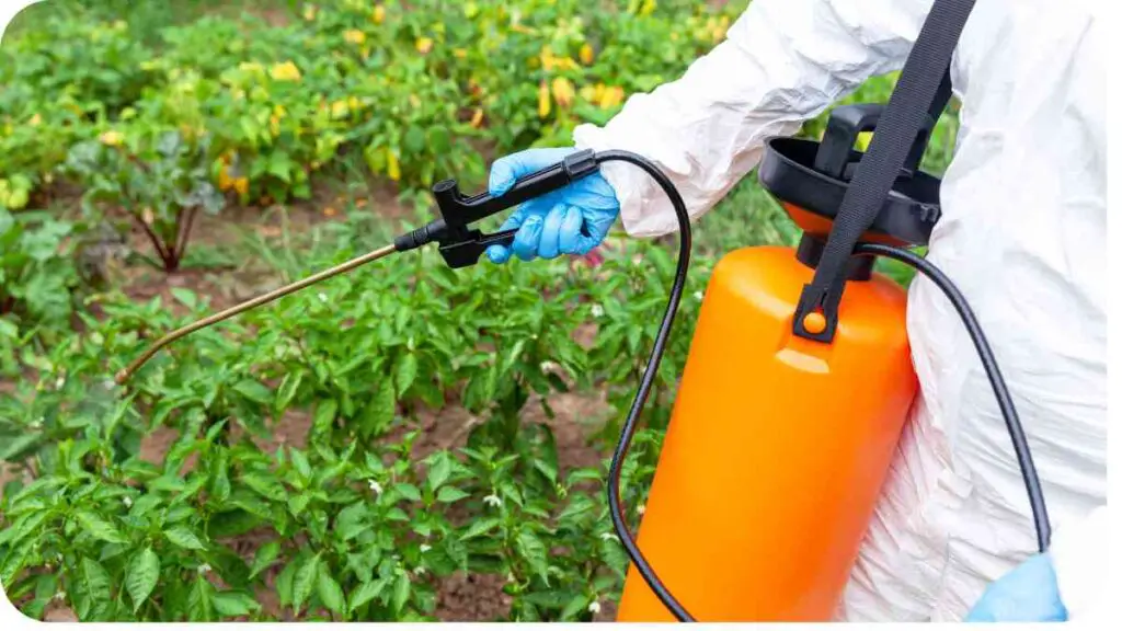 a person in a white protective suit using an orange sprayer to spray plants